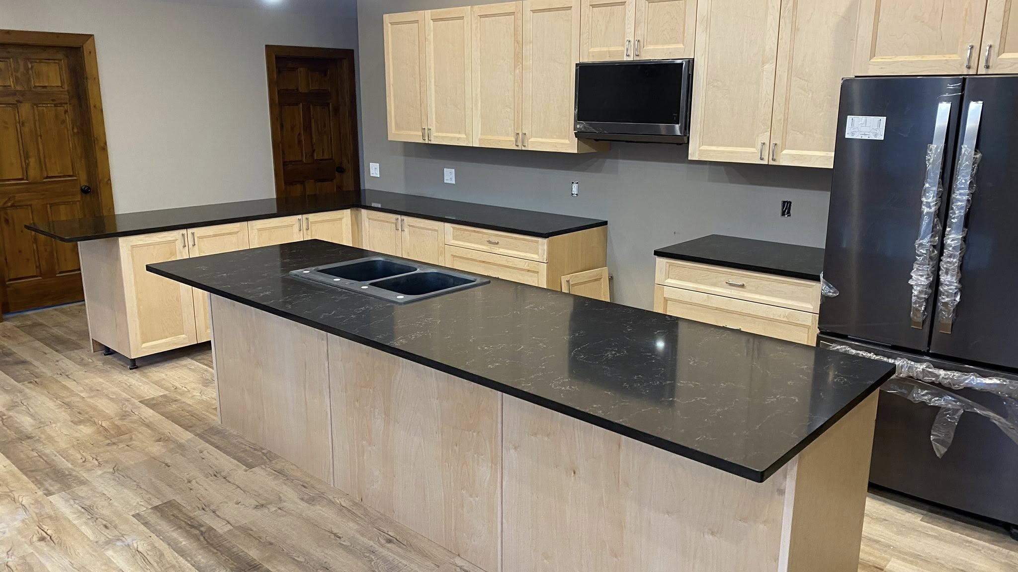 Open-plan kitchen with a black granite waterfall island and natural maple cabinets.