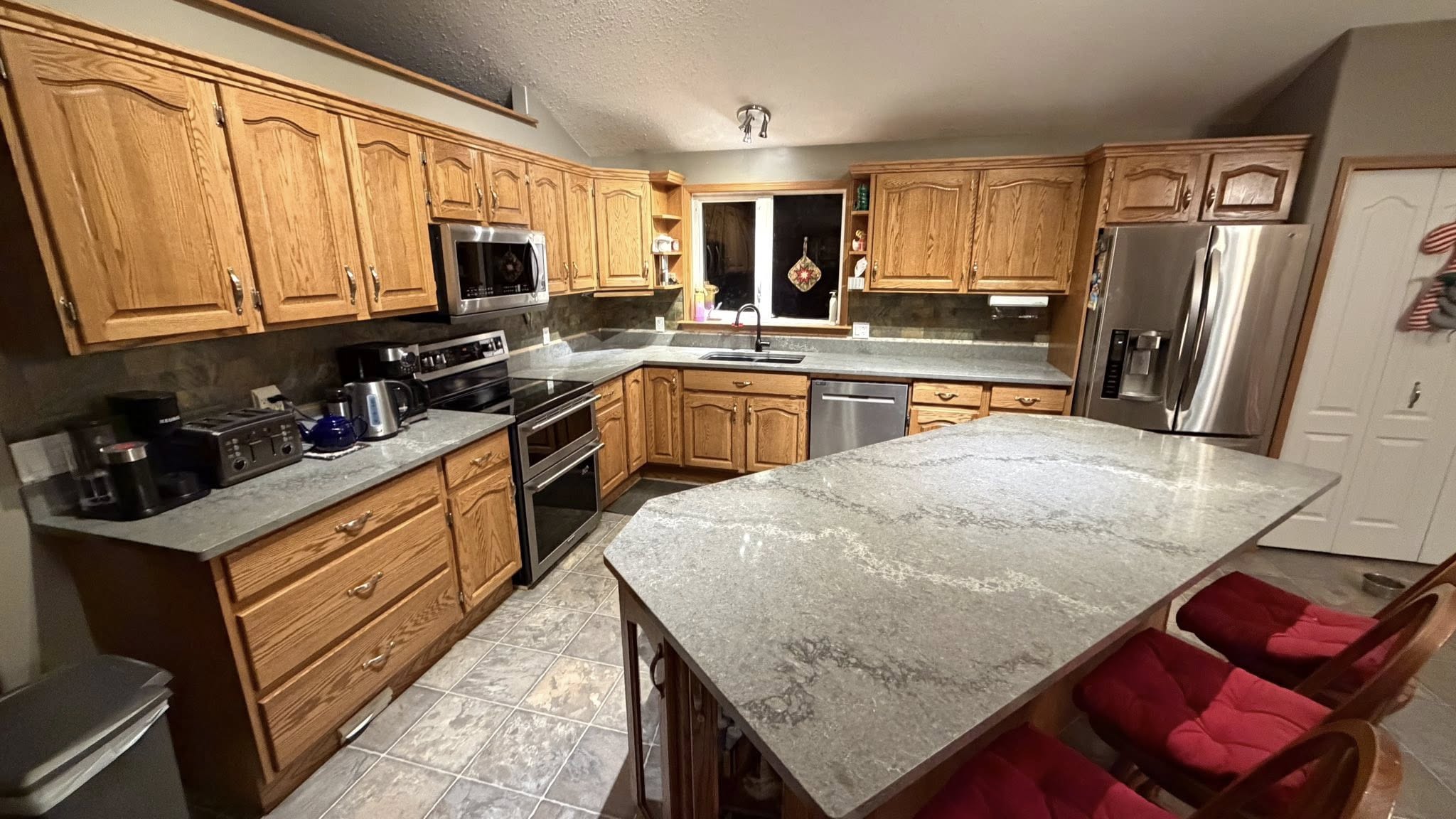 Oak kitchen with a light grey granite island and stainless steel appliances.